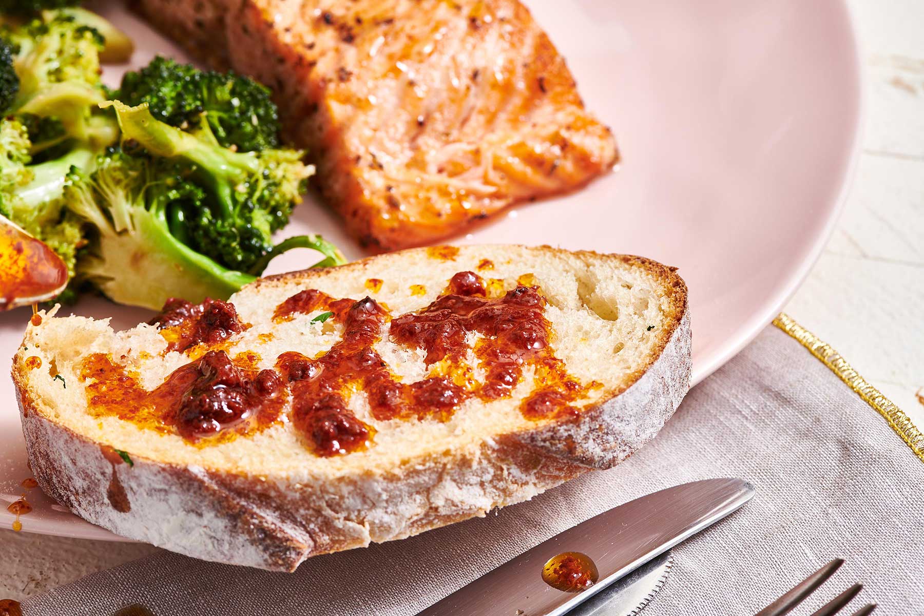 Toasted bread with harissa sauce on plate with salmon and broccoli.