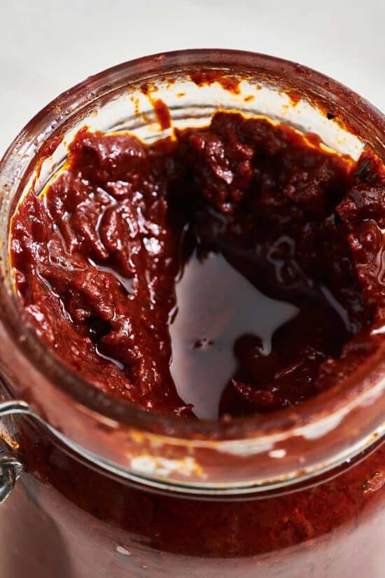 Dark red Harissa Sauce in a glass jar.