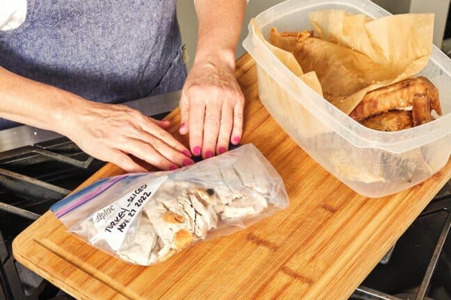Woman pressing the excess air out of a Ziploc filled with slices of cooked turkey.