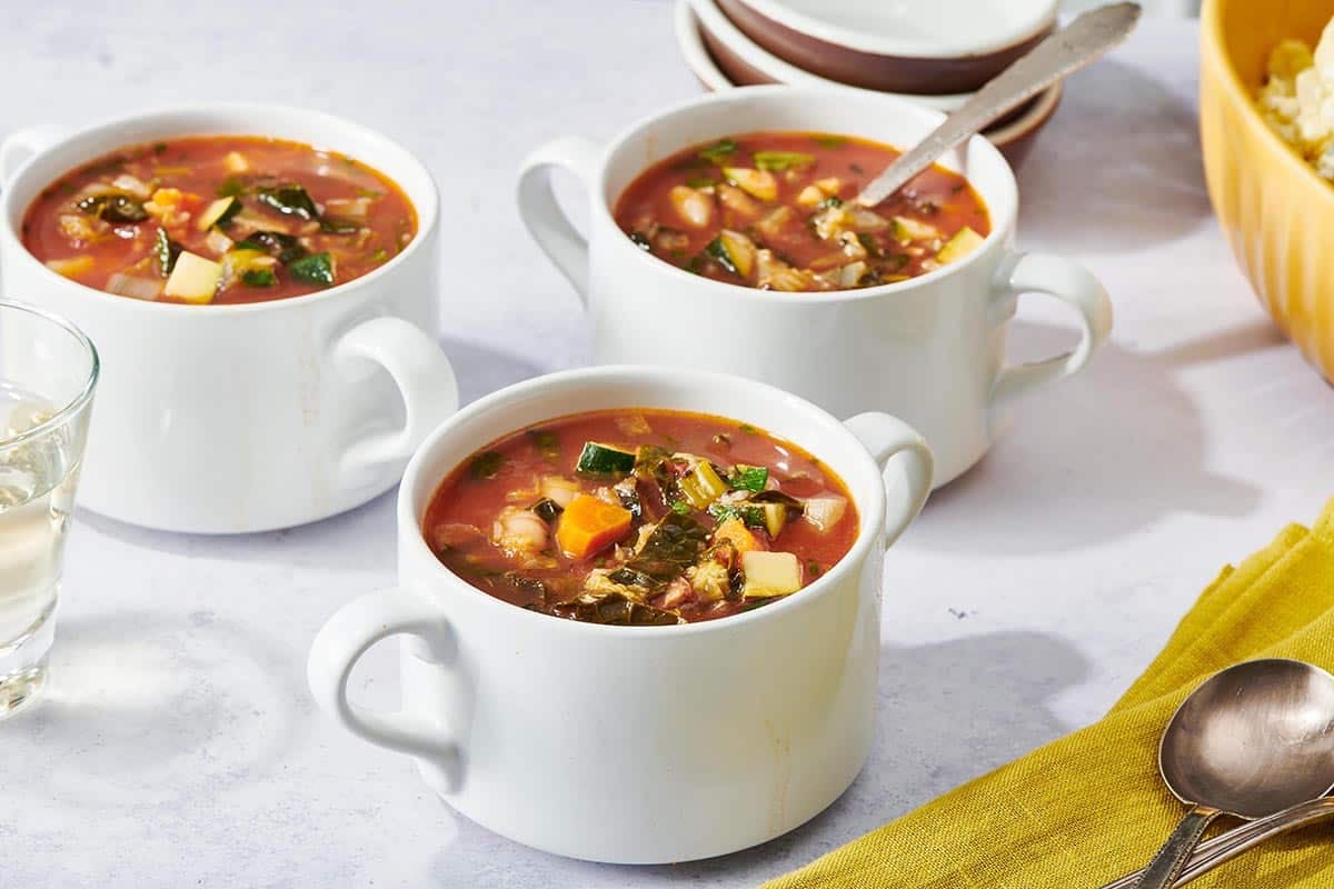 Three handled, white bowls of Minestrone Soup.