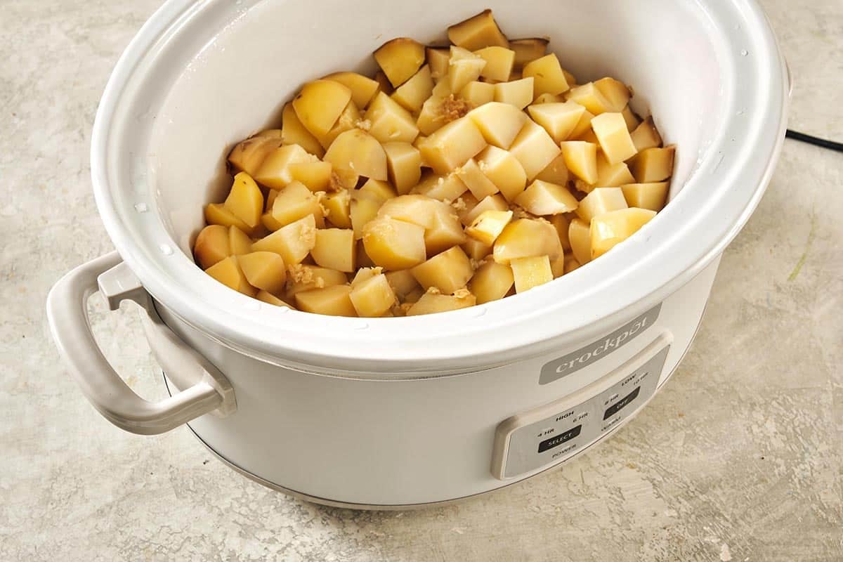 White Crock Pot full of diced potatoes.