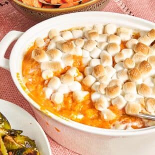Baking dish of Sweet Potato Casserole with Marshmallows on a pink tablecloth.