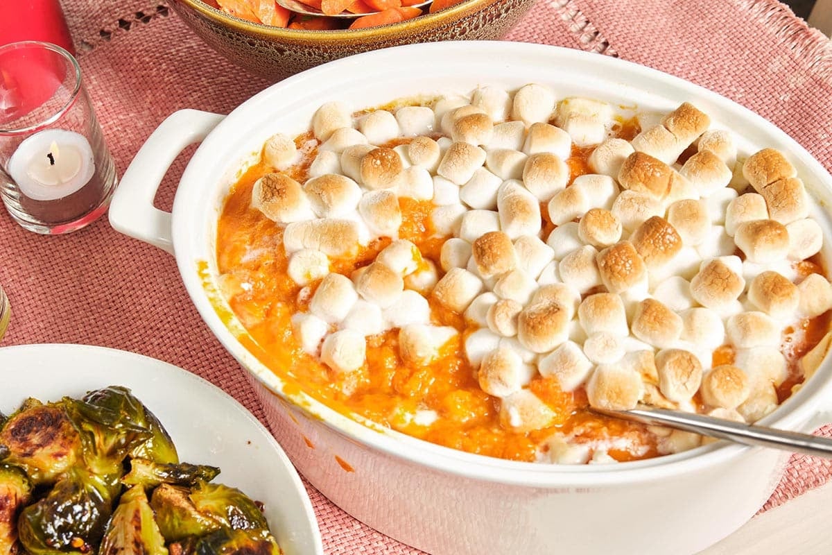 Baking dish of Sweet Potato Casserole with Marshmallows on a pink tablecloth.