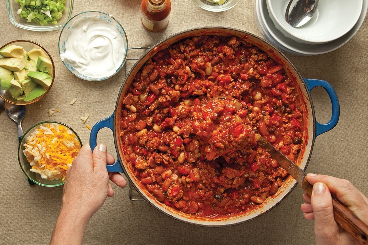 Serving turkey chili from pot next to chili toppings.