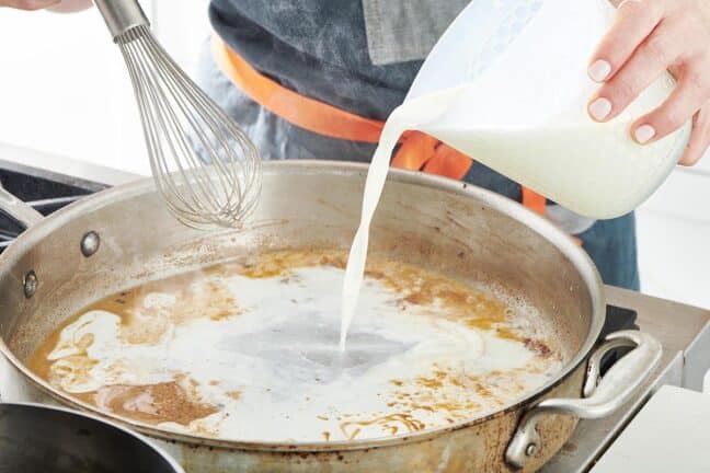 Pouring milk into a skillet of flour and pan drippings.