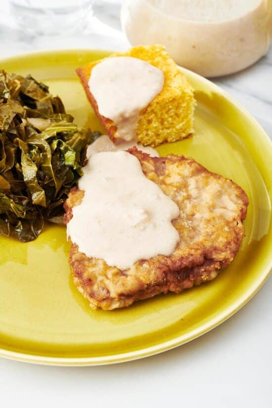 Plate with green, chicken fried steak, corn bread, and white gravy.