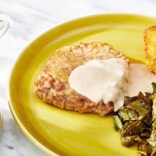 Chicken fried steak with white gravy on a yellow plate.
