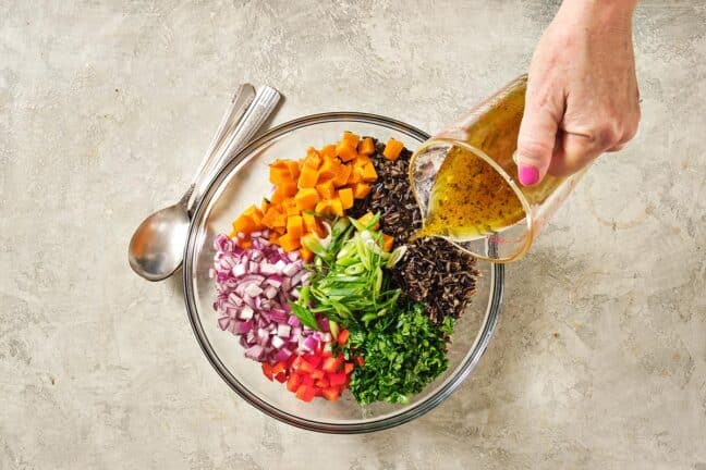 Woman pouring dressing onto a bowl of unmixed, colorful ingredients.