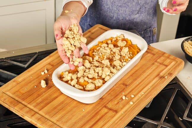 Woman placing streusel topping onto Butternut Squash Casserole.
