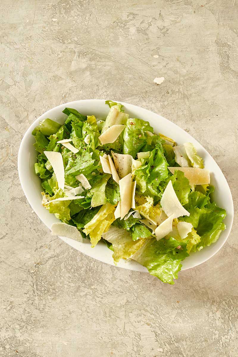 Oblong, white bowl of Escarole Salad on a textured surface.