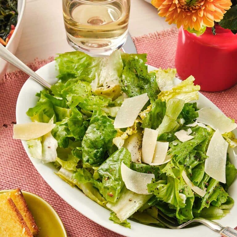 Bowl of Escarole Salad set next to a glass of white wine, bread, and flowers.