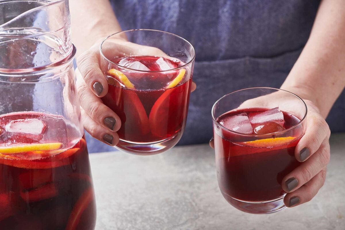 Woman holding two small glasses of Hibiscus Cocktail.