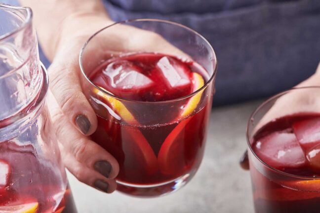 Woman holding a small glass of Hibiscus Cocktail.