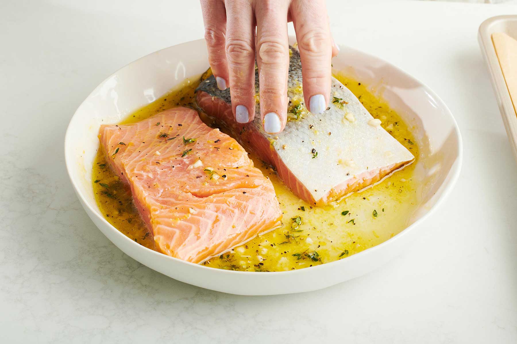Woman's hand placing salmon into a marinade mixture.