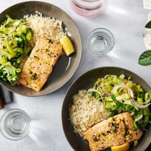 Two dark plates of Salmon, salad, and rice on a white table.