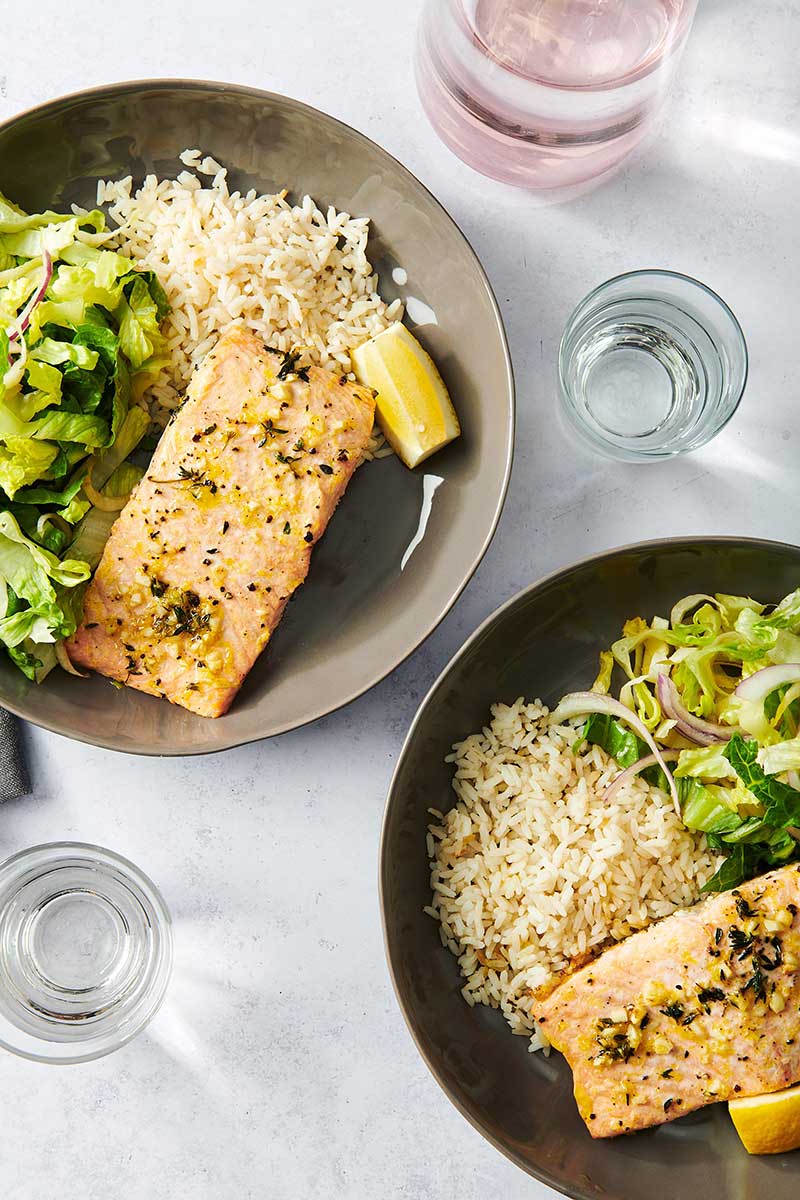 Two plates of baked salmon with rice and salad.