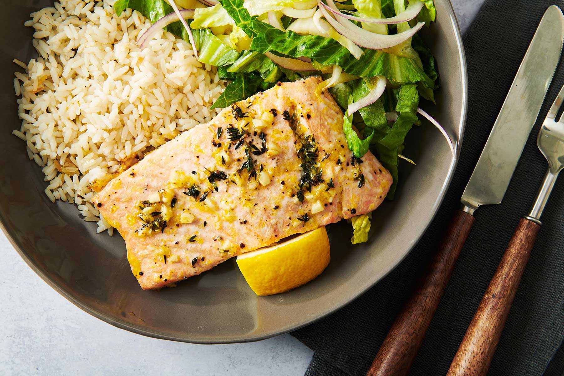 Marinated salmon on a plate with rice, salad, and a lemon wedge.