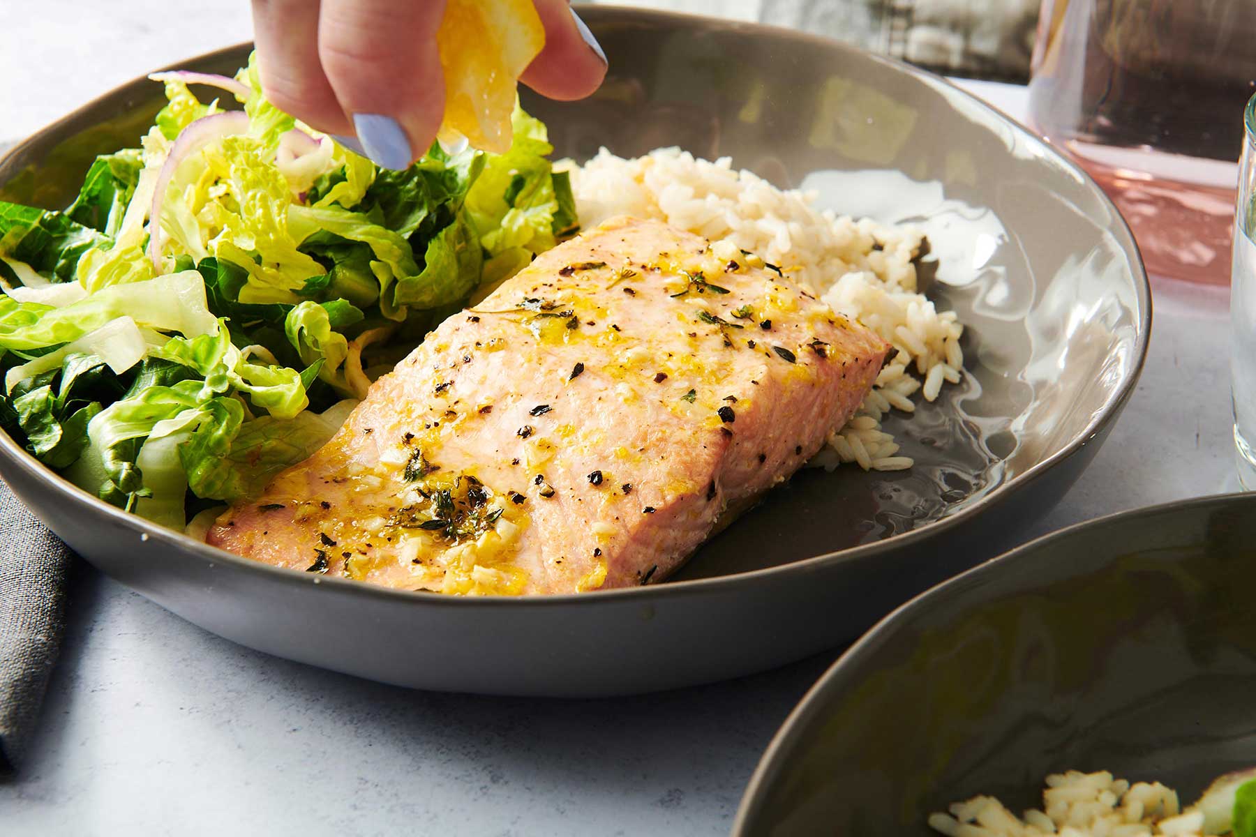 Hand squeezing a lemon wedge onto a Salmon filet.