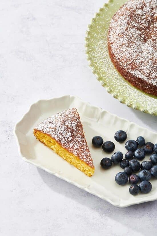 Slice of Orange Cake and blueberries on a white plate with fluted edges.
