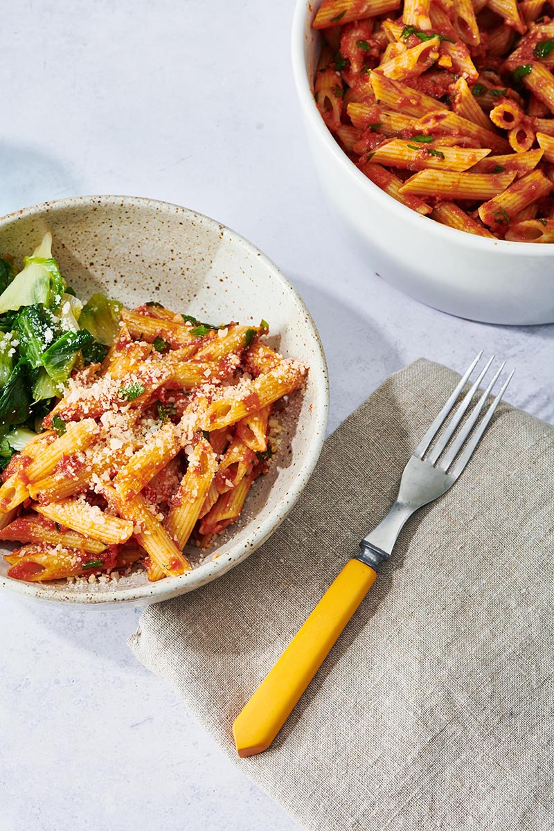 Plate with Penne all’Arrabbiata next to a yellow fork.