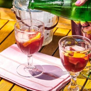 Green bottle pouring sparkling water into glasses of red sangria.