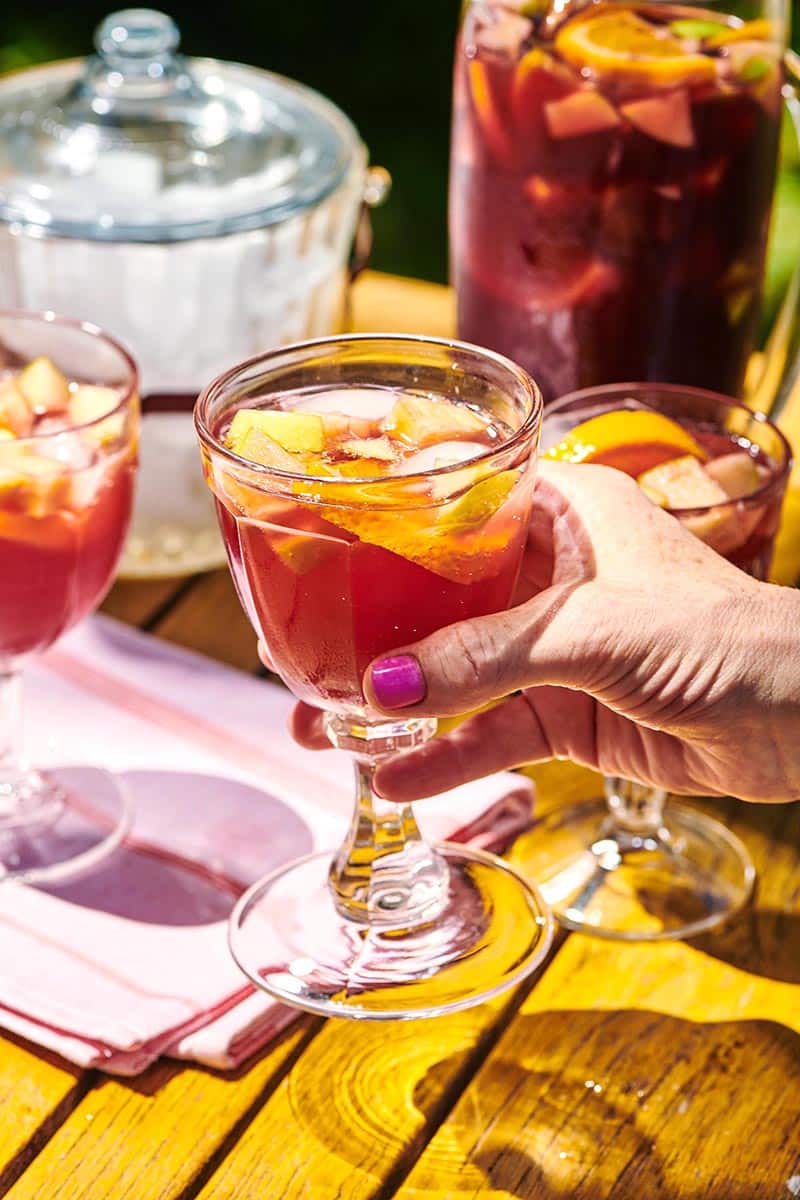 Woman holding glass of red sangria at picnic table.