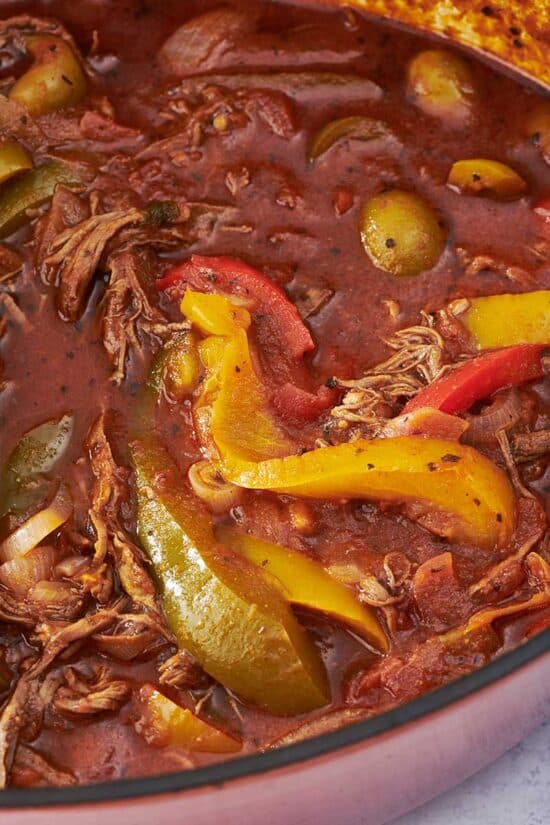 Ropa Vieja in a pan with peppers, olives, and onions.