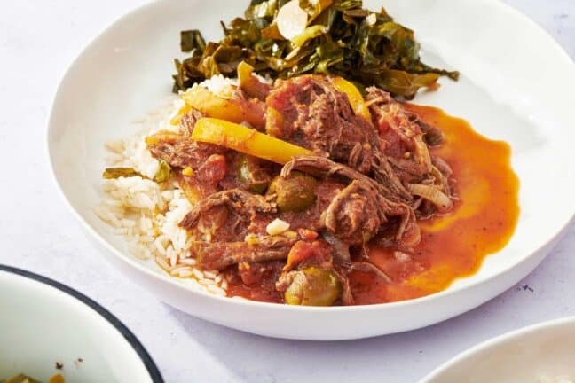 Ropa Vieja with peppers and olives on a white plate.