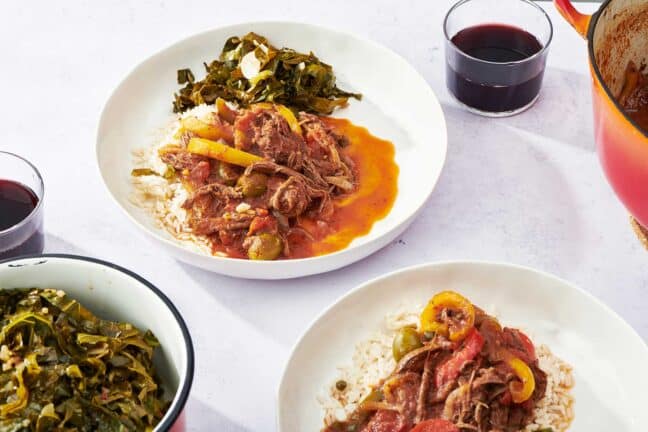 Two plates of Ropa Vieja and greens on a white table.