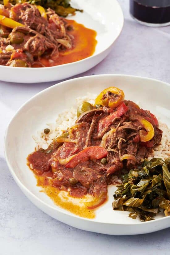 Ropa Vieja on rice on a white plate with greens.