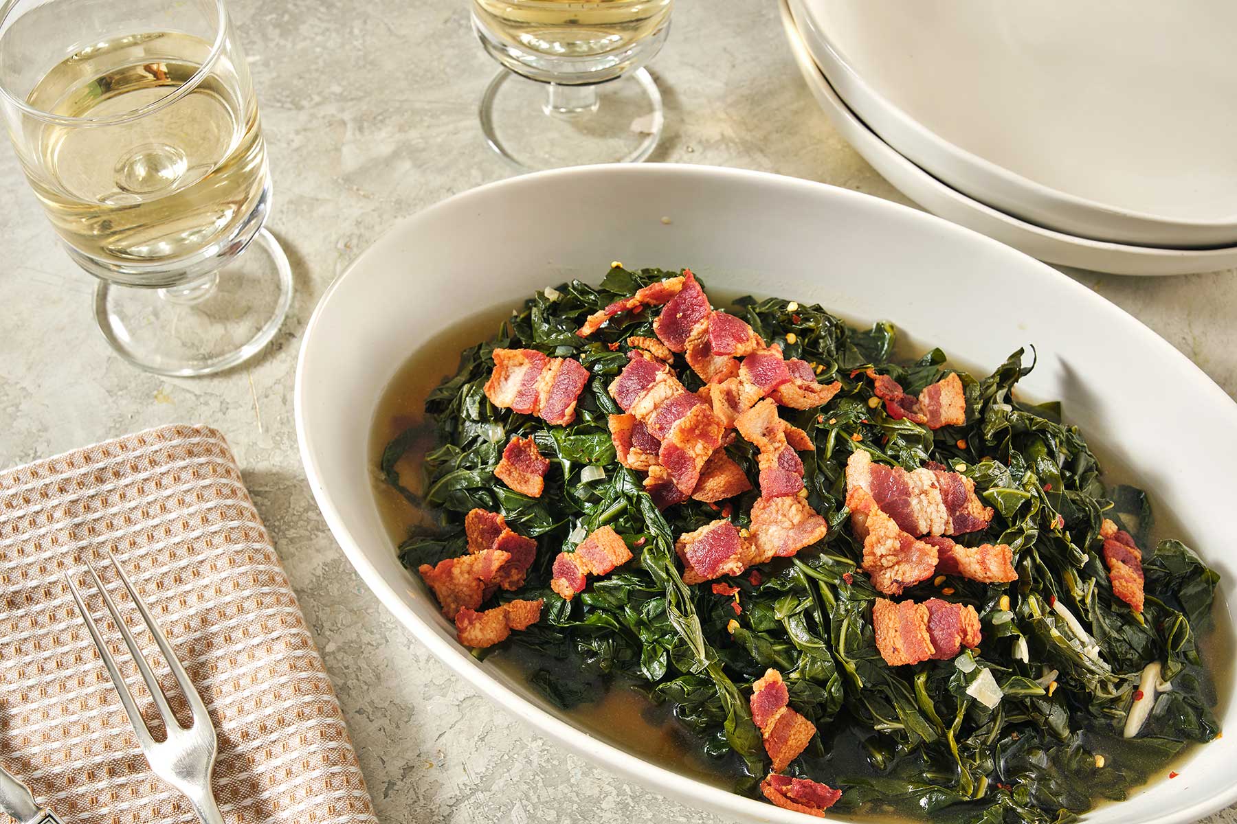 Southern Collard Greens with Bacon on a table with two glasses of white wine.