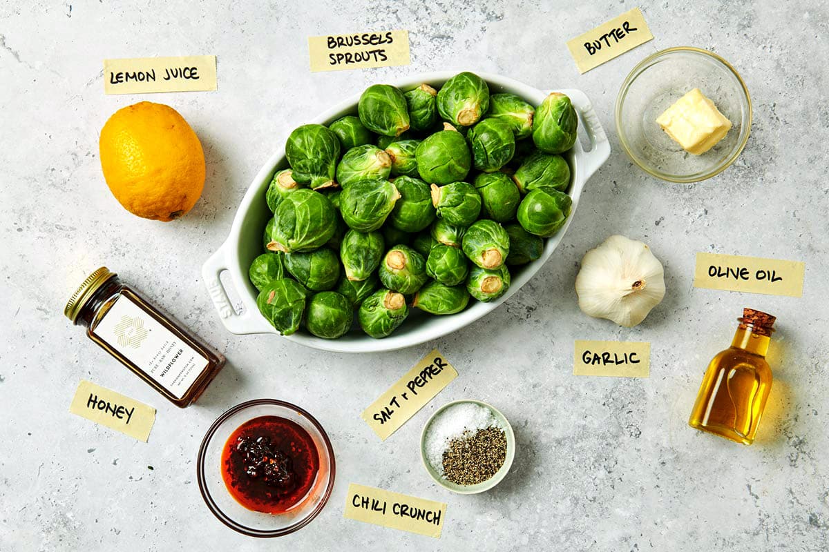 Brussels sprouts, garlic, chili crisp, and other ingredients on white table.