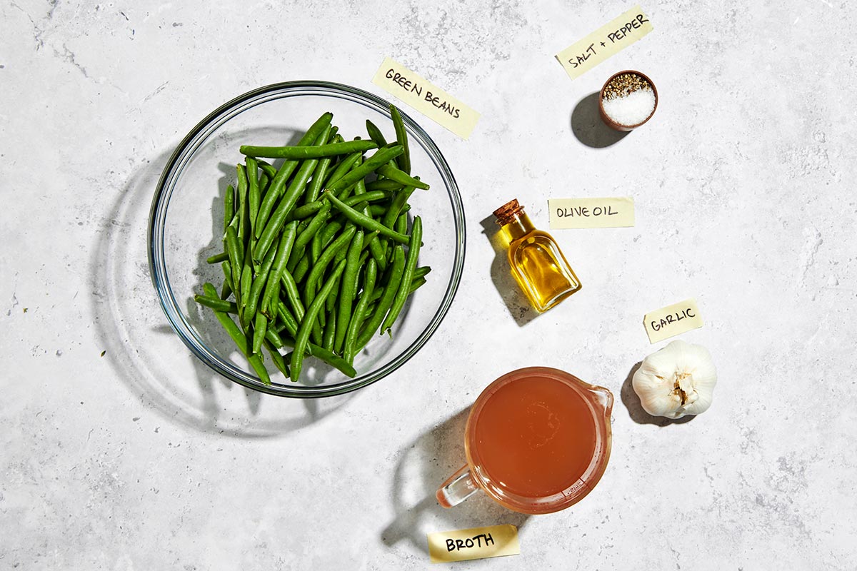 Fresh green beans, broth, oil, and garlic on marble table.