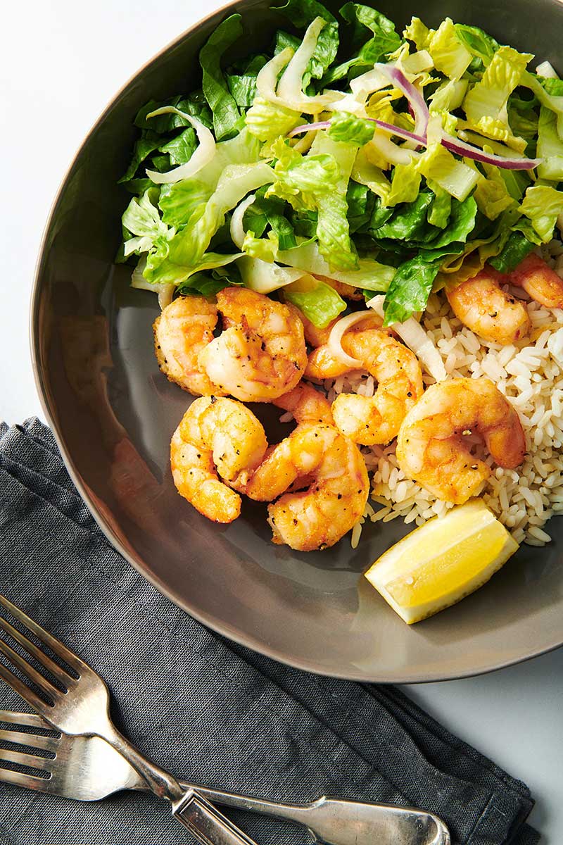 Air-fried shrimp on brown plate with rice, green, leafy salad, and lemon wedge.