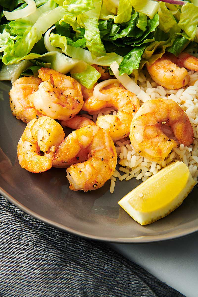 Air-fried shrimp on brown plate with rice and green, leafy salad.
