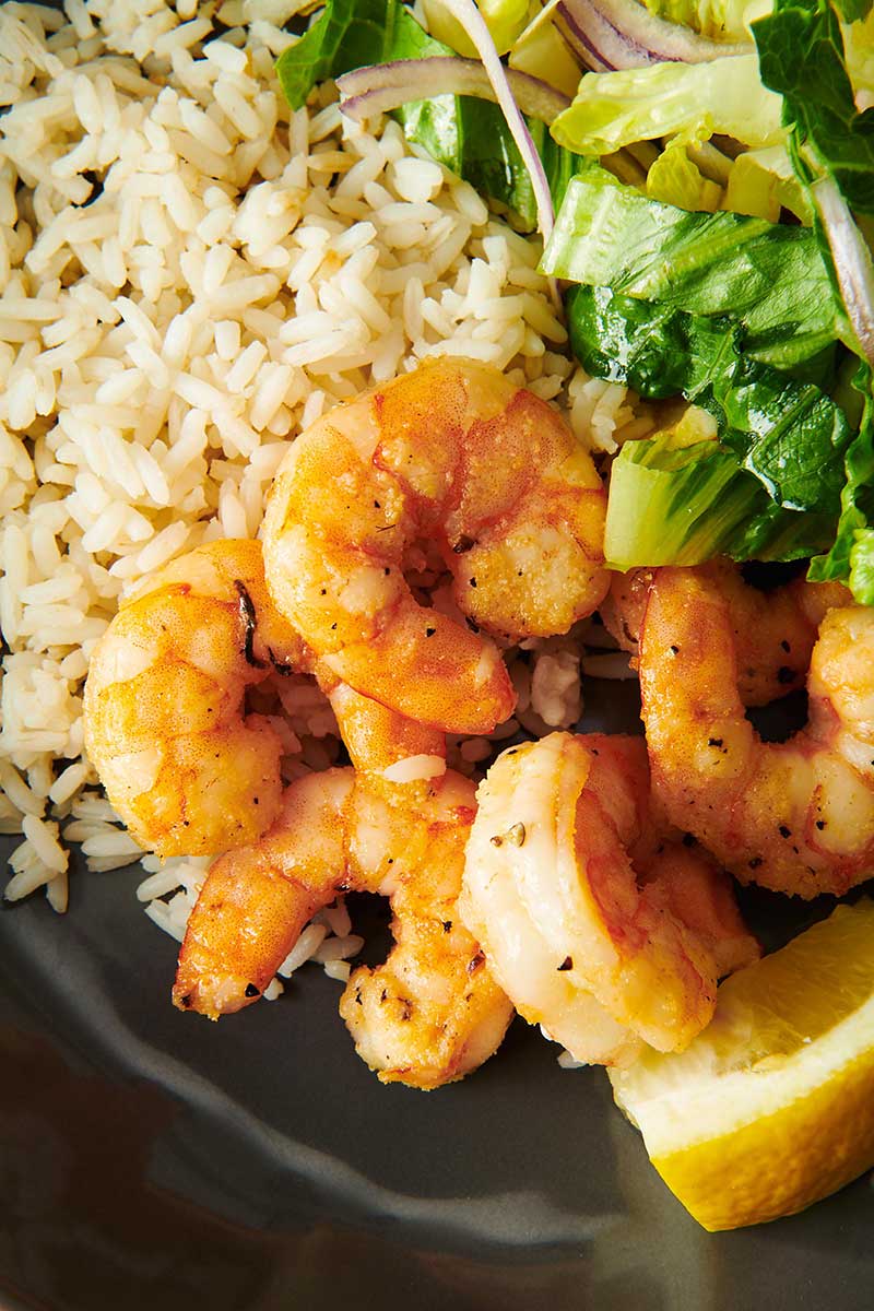 Air-fried shrimp with rice and salad on dark plate.