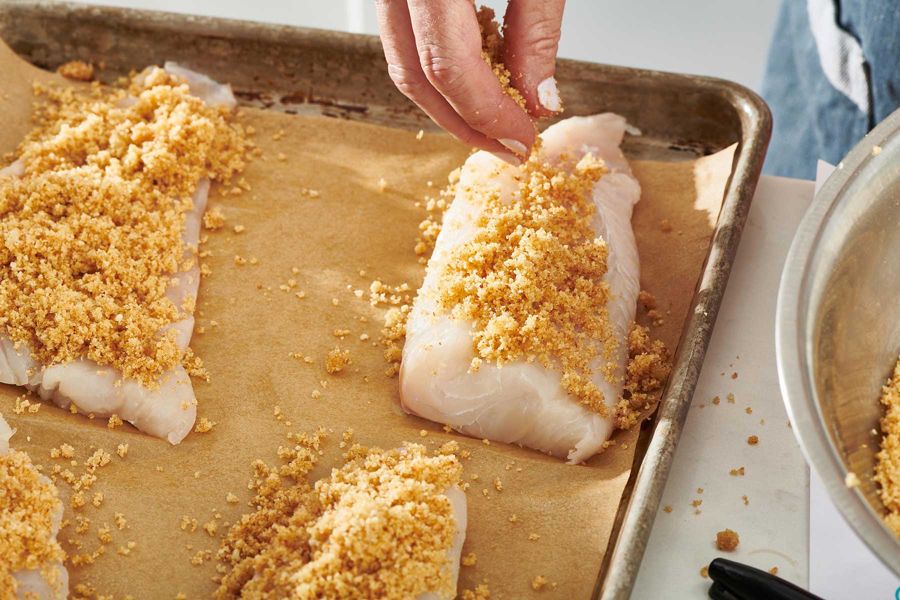 Sprinkling breadcrumb topping on haddock fillets.