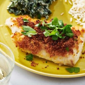 Baked Haddock garnished with fresh parsley on yellow plate.