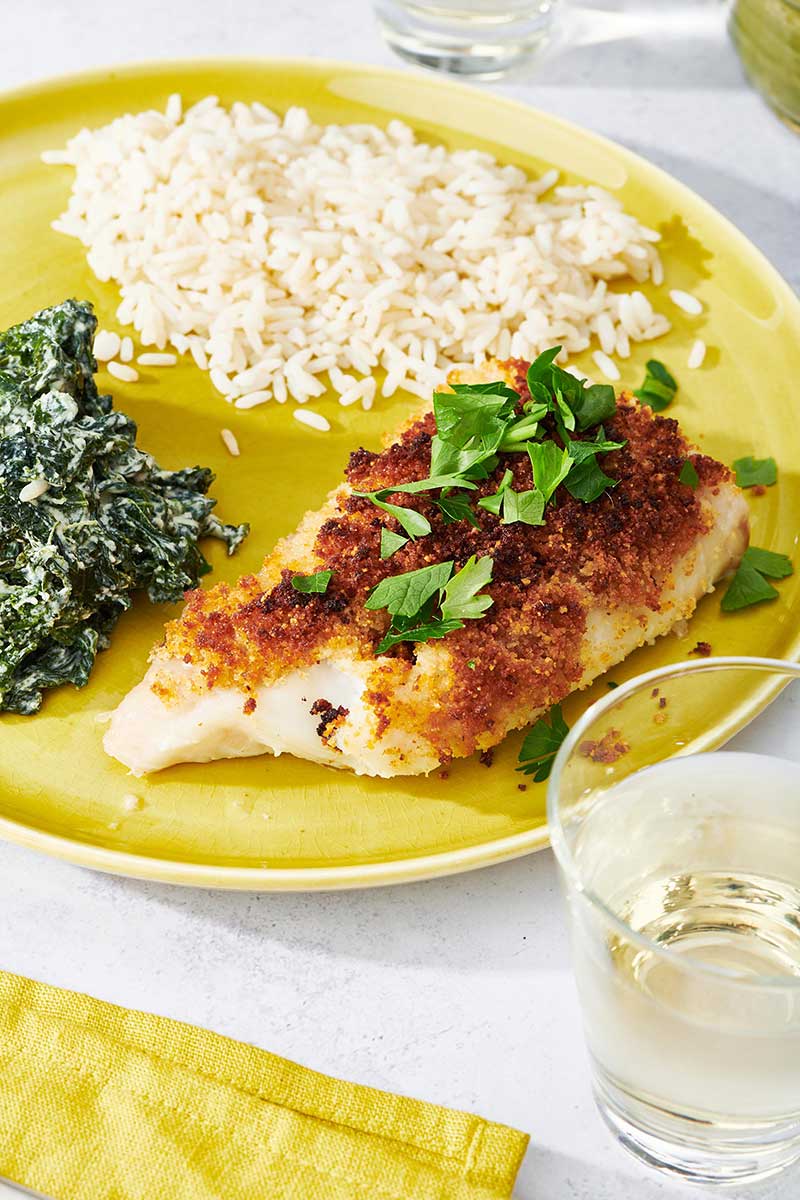 Baked Haddock on yellow plate with creamed kale and a side of white rice.