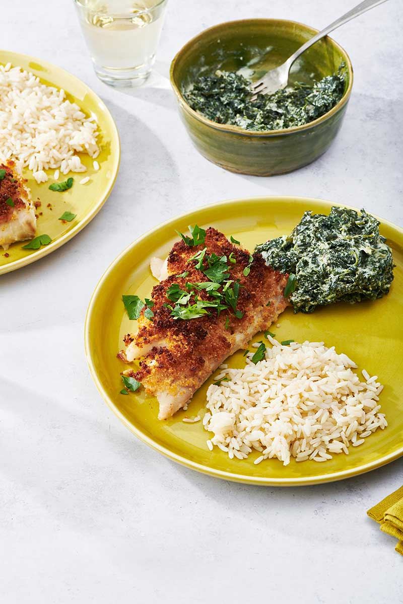 Baked Haddock on yellow plate with creamed kale and white rice.