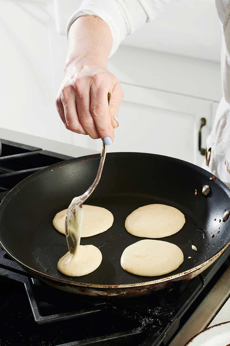 Woman spooning pancake batter into hot skillet.
