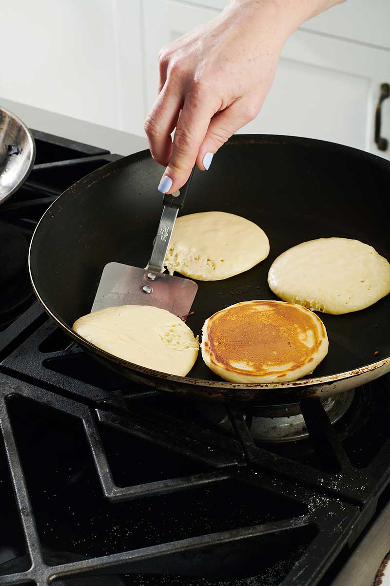 Woman flipping pancakes in pan with spatula.