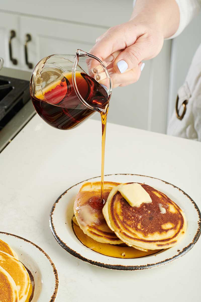 Woman pouring syrup over homemade pancakes