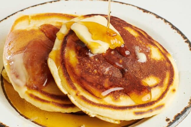 Maple syrup drizzled over homemade pancakes with butter