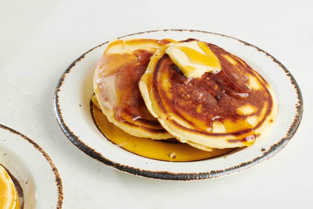 Plate of pancakes topped with syrup and butter.