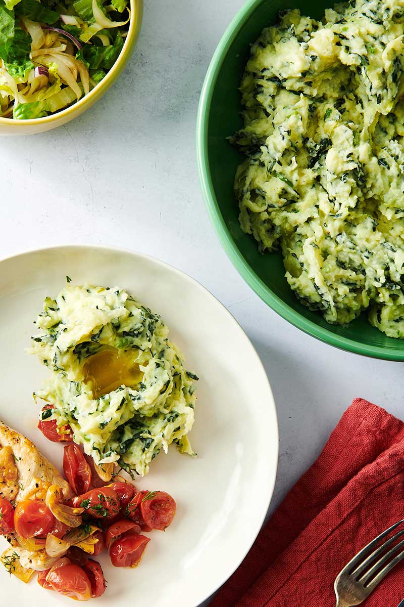 Plate with Colcannon, chicken, and tomatoes next to a bowl of colcannon.