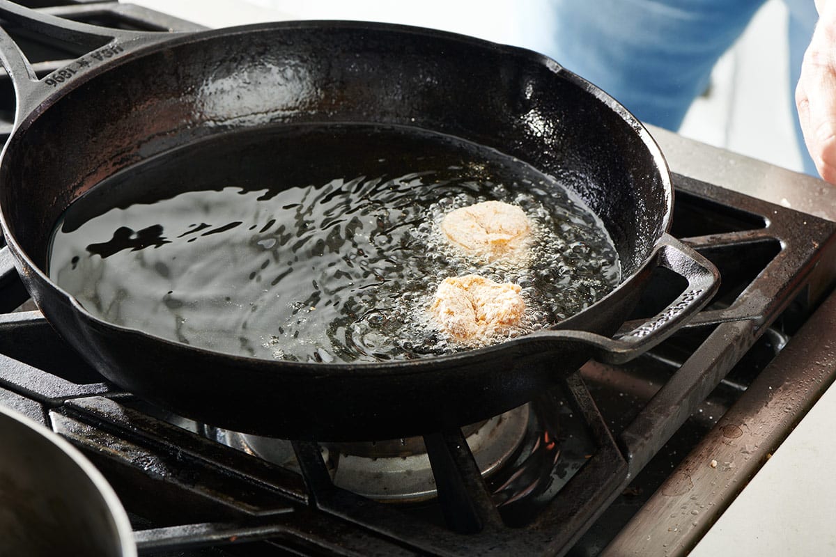Two shrimp frying in bubbling oil in a cast iron pan.