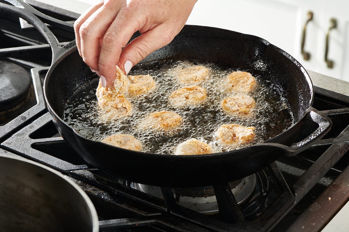 Woman drops shrimp into pan filled with bubbling oil with other shrimp.