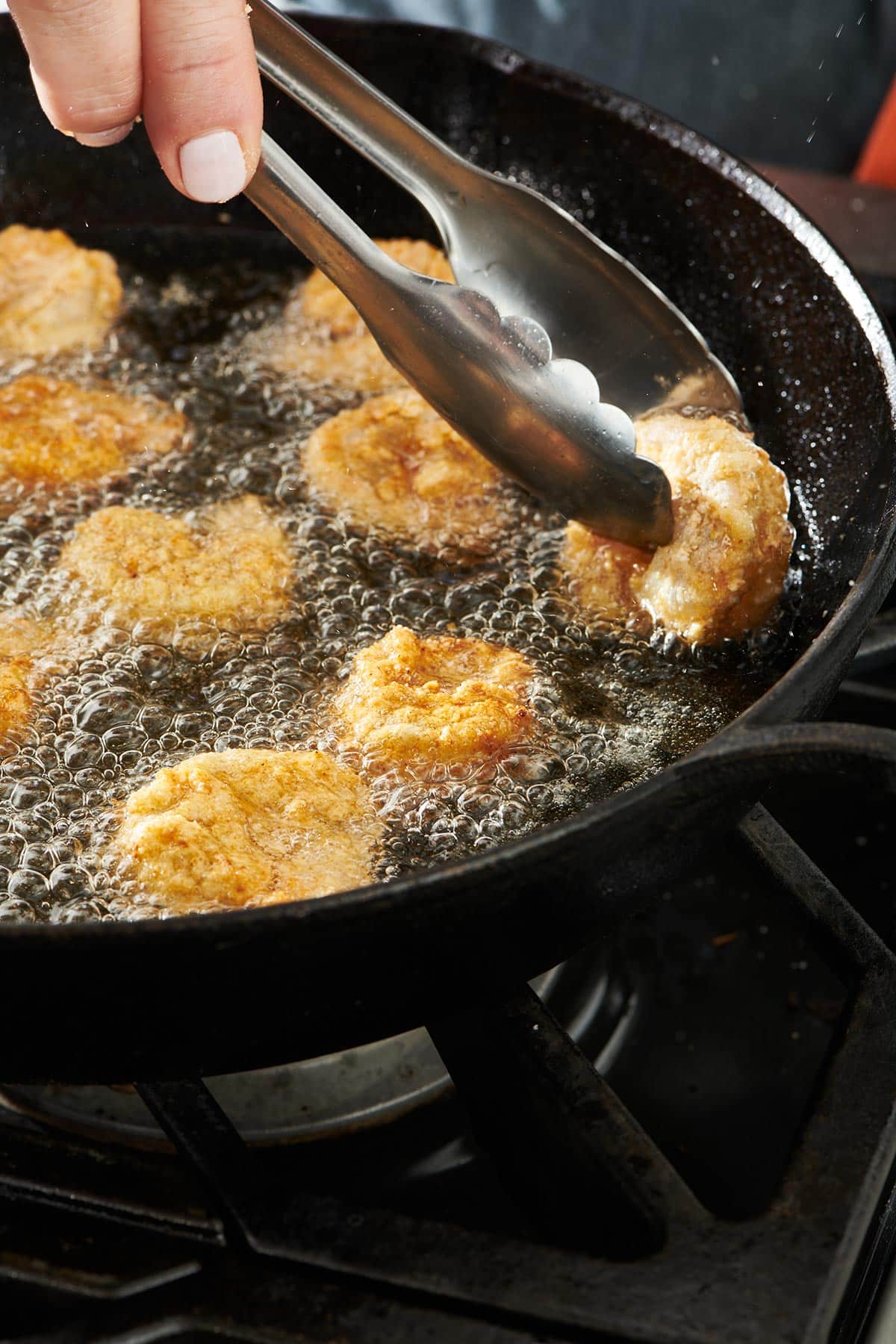 Breaded shrimp frying in bubbling oil in a cast iron pan.