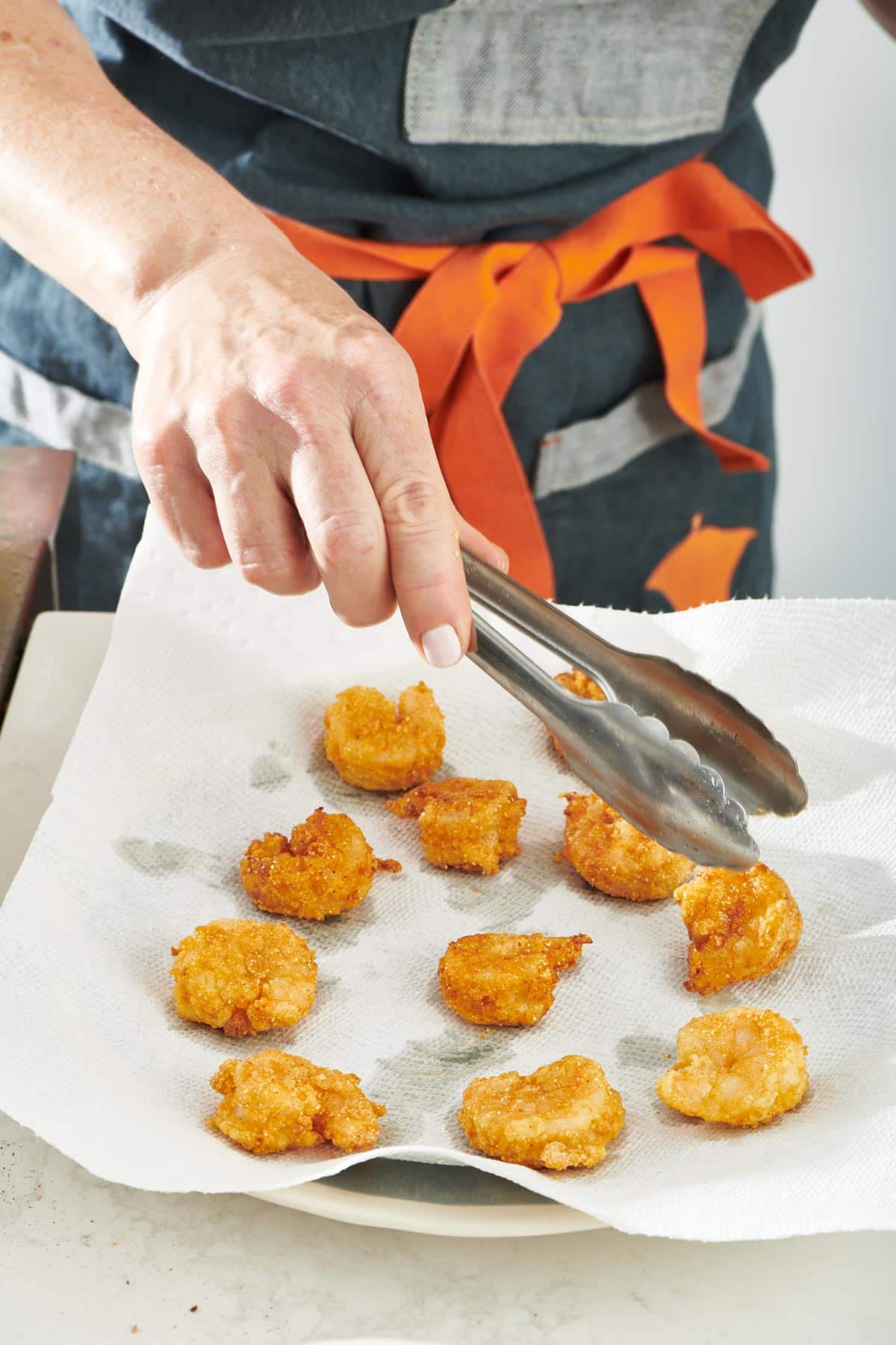 Woman using tongs to place fried shrimp on paper towels.